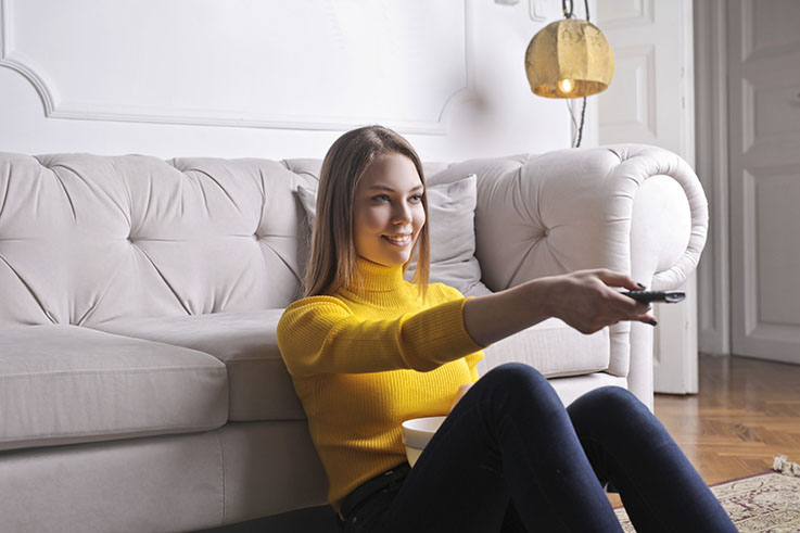 A young adult sitting on the living room floor holding a remote